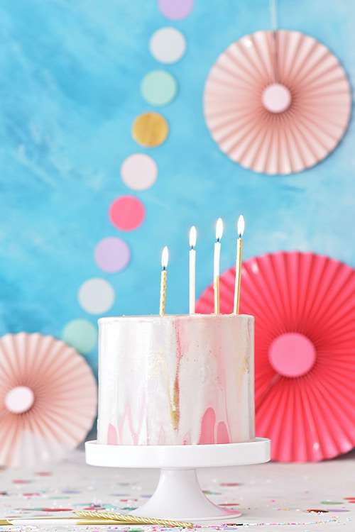 Tortas su žvakutėmis ir šiltas, linksmas dekoras fone.
