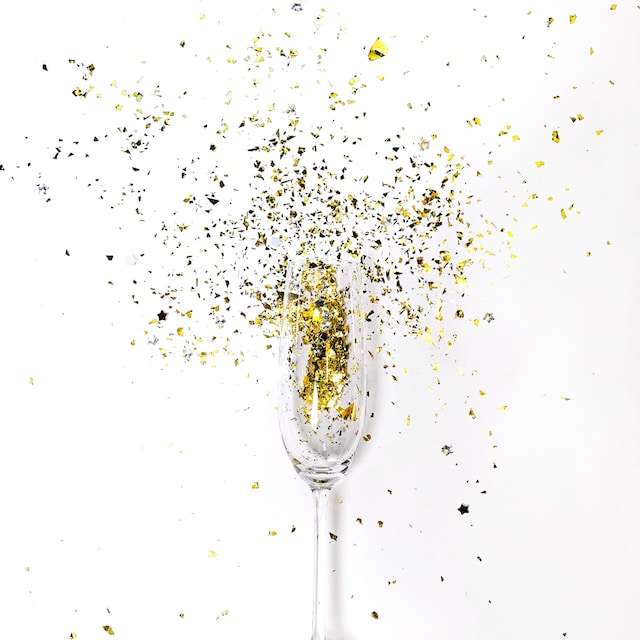 Šampano taurė su auksiniais ir sidabriniais konfeti.