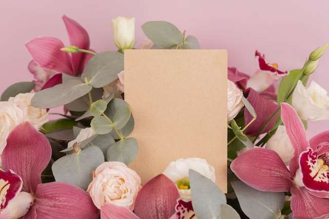 Natūralios spalvos atvirukas su rausvomis orchidėjomis ir baltomis rožėmis prieš rožinį foną.