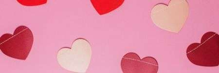 Raudonos ir baltos širdelės ant rožinio fono, sukurdamos romantišką atmosferą.