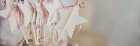 Baltos žvaigždės su rožiniais kaspinėliais stiklainyje ant šviesaus paviršiaus.