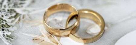 Aukso žiedai ant geometrinių raštų fono su baltų gėlių kontūrais.